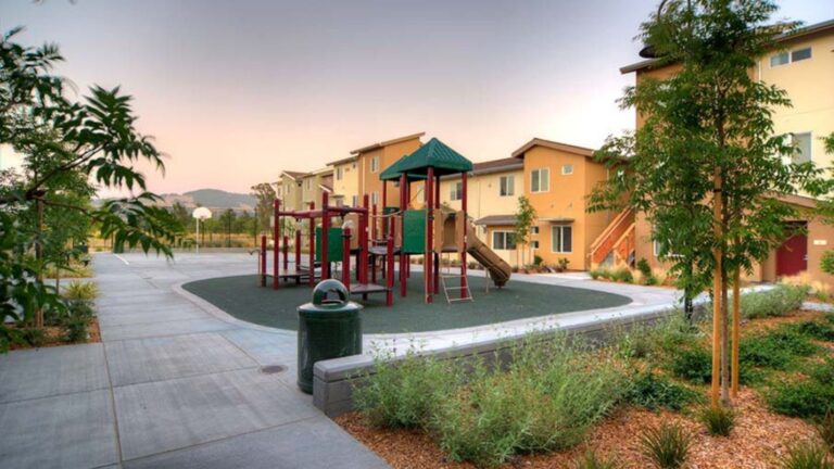 A housing complex with a playground and beautiful landscaping.