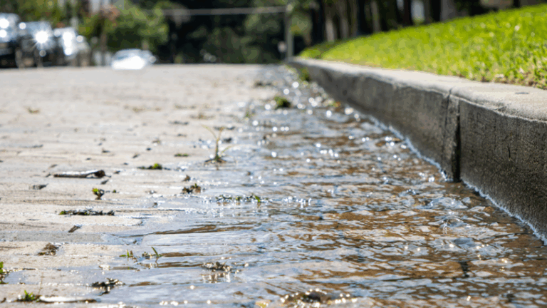 A flowing puddle of water on a stone path near a curb.